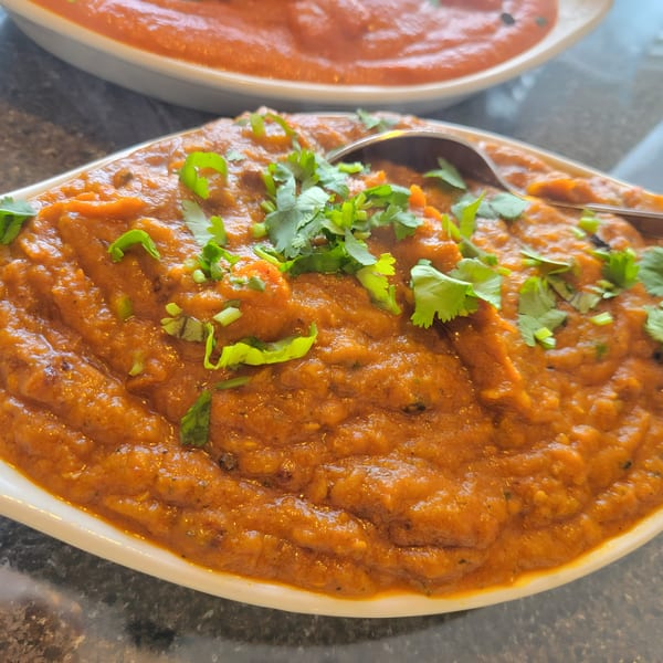 Close-up of a bowl of Indian curry, garnished with fresh cilantro, with a spoon in it.