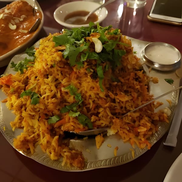 A large serving of Indian biryani rice with cilantro and cashews, alongside a side of curry.