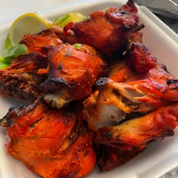 Close-up of vibrant red Indian Tandoori chicken pieces with charred edges, garnished with lemon wedges.