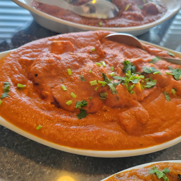 Close-up of a Taj Cuisine Indian dish, a rich orange curry with green herbs in a white bowl.