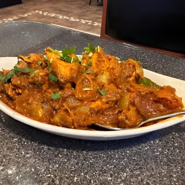 A white oval dish filled with a rich orange-brown Indian curry, garnished with fresh cilantro.