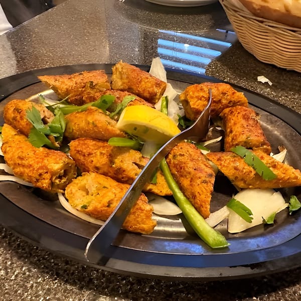 Taj Cuisine Indian Pak Food's platter of golden-brown fried appetizers with lemon, onions, and cilantro.