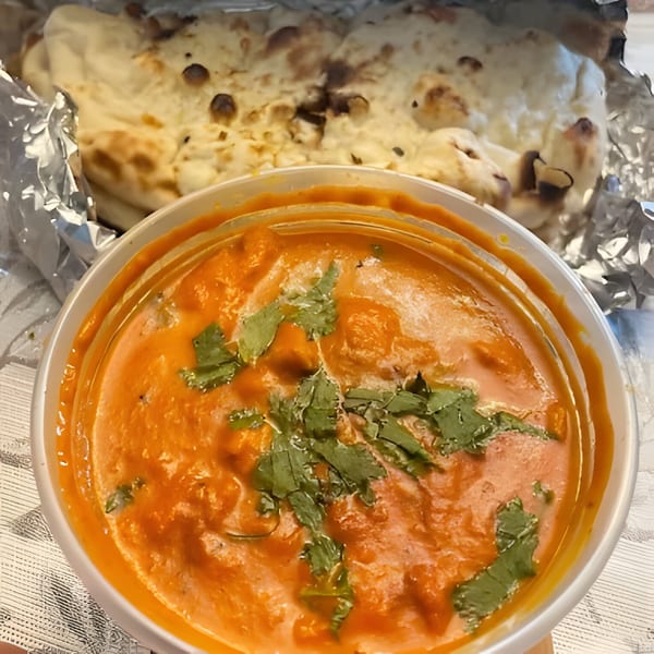 Indian butter chicken with cilantro in a bowl, with naan bread wrapped in foil behind it.