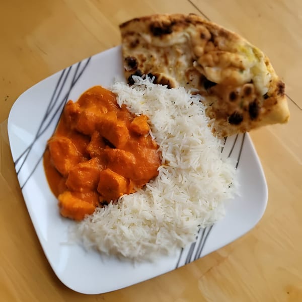Indian butter chicken with white rice and naan bread on a white plate with black stripes.